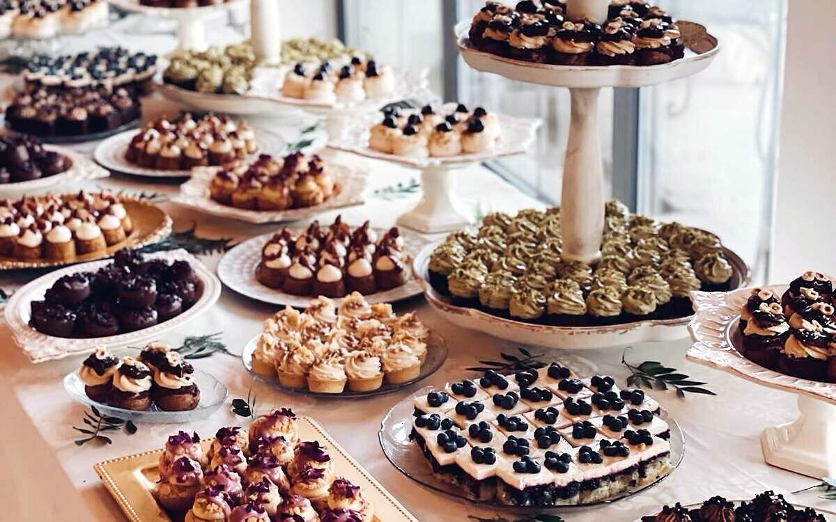 Candy bar cu etajere și platouri cu deserturi mici, lângă o fereastră