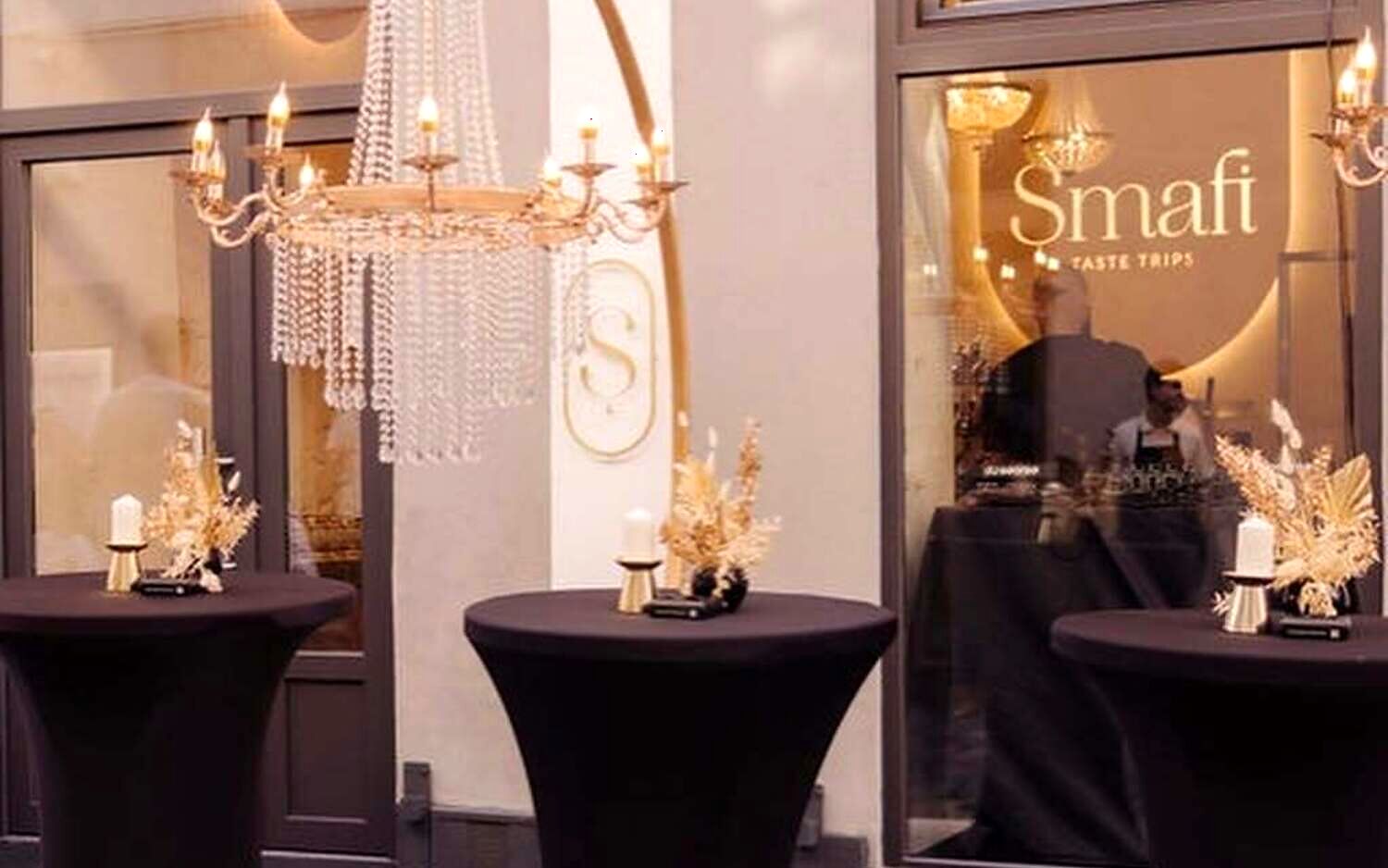 Intrarea în cake shop-ul Șmafi, seara, cu monograma aurie pe geam și candelabru înăuntru