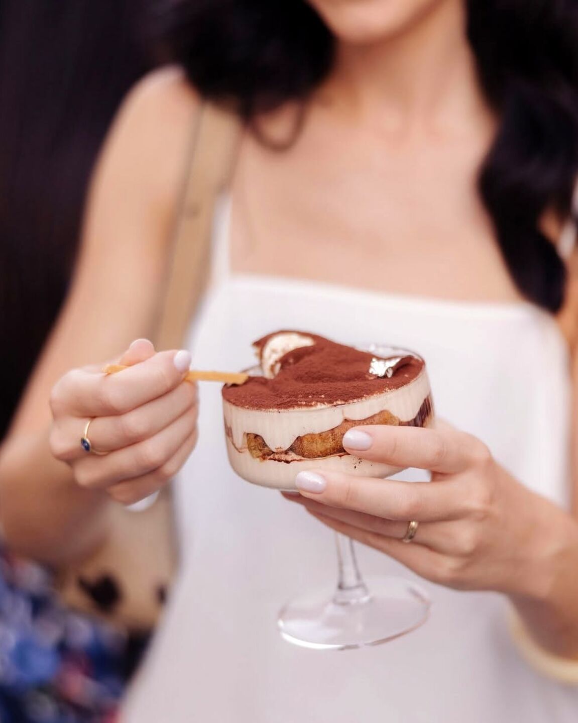 Mâini ținând un pahar cu tiramisu, cu lingurița aurie deasupra, în cake shop-ul Șmafi