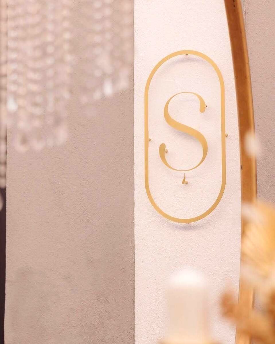 Monograma aurie Ș, pe peretele de var texturat al cake shop-ului