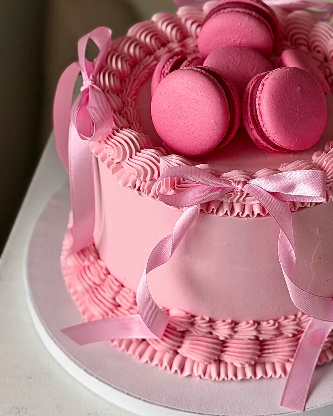 Tort roz cu cremă modelată, funde de satin și macarons