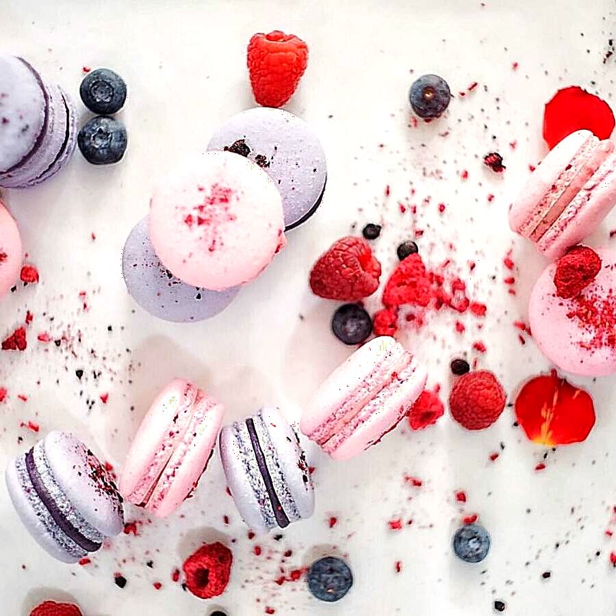 Macarons colorați împrăștiați lângă zmeură și afine