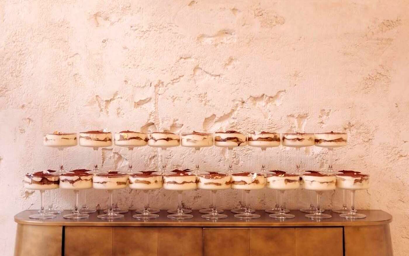 Pahare cu tiramisu aliniate pe o comodă de alamă, sub peretele de var